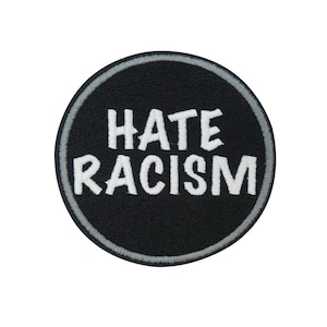 Può includere: Una toppa rotonda nera con la scritta bianca ricamata "HATE RACISM". La toppa ha un bordo grigio ed è posta su uno sfondo bianco. Questa toppa è adatta per giacche, borse o altri articoli in tessuto.