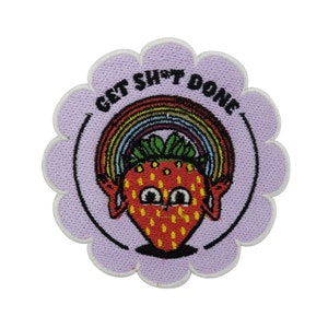 Könnte beinhalten: Ein lila gestickter Patch mit einem weißen Umriss in Form einer Blume. Der Patch zeigt eine rote Erdbeere mit einem grünen Blatt oben und einem Regenbogen, der sich darüber wölbt. Der Text "GET SH*T DONE" ist in einem weißen Kreis um die Erdbeere geschrieben.