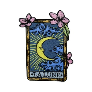 May include: A yellow crescent moon with a blue sky and clouds in a gold frame with the text "LA LUNE" at the bottom. The frame is decorated with pink flowers.