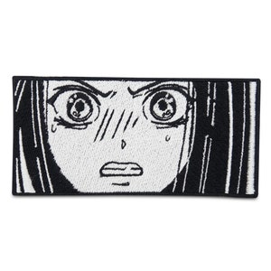 May include: Black and white embroidered patch of a woman's face with large eyes and a surprised expression.