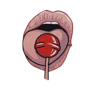 Może przedstawiać: Naszywka haftowana z różowymi ustami, z których wystaje czerwony lizak. Lizak ma biały wzór w kształcie spirali.