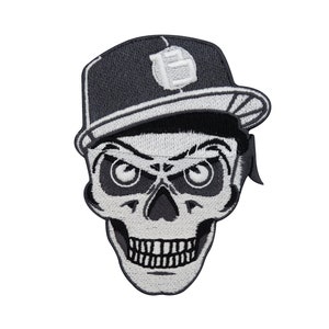 May include: Black and white embroidered patch of a skull wearing a black baseball cap with the number "15" on it.