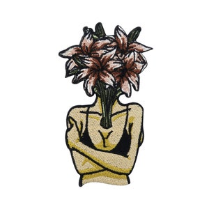 Pode incluir: Etiqueta bordada com uma figura estilizada com um buquê de flores rosa e castanhas a crescer da sua cabeça. A figura está a usar um top halter preto e tem os braços cruzados.