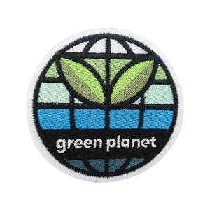 Puede incluir: Un parche circular blanco con una planta verde que crece de un globo azul y verde. El texto "green planet" está escrito en negro debajo del globo.