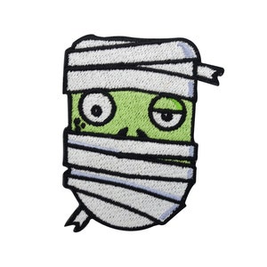 May include: A green cartoon mummy with white bandages and black eyes. The mummy is smiling and has a mischievous look on its face.