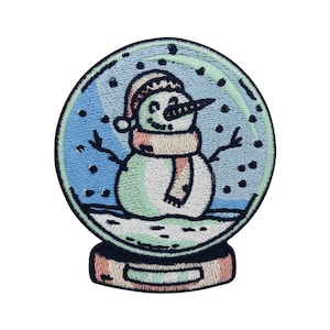 Könnte beinhalten: Ein blauer und grüner gestickter Aufnäher mit einem Schneemann in einer Schneekugel. Der Schneemann trägt einen rot-weißen Hut und einen rosa-grünen Schal.