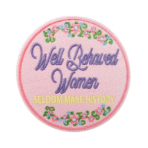 May include: A circular, pink embroidered patch featuring the text "Well Behaved Women Seldom Make History" in purple and yellow. The patch has a pink stitched border and floral embroidery.