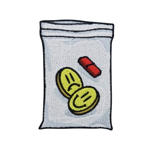 Pode incluir: Uma bolsa de plástico branca com fecho de correr preto. A bolsa contém duas pílulas amarelas com um desenho de cara sorridente e uma pílula vermelha.