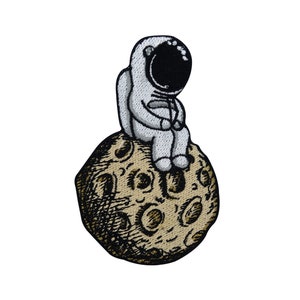 Könnte beinhalten: Ein gestickter Aufnäher mit einem weißen Astronauten, der auf einem braunen Mond mit Kratern sitzt.