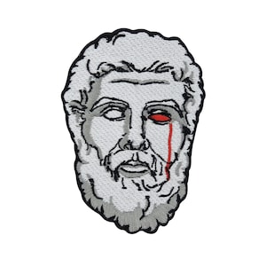 Op de afbeelding: Gestikte patch van een wit marmeren buste van een man met een rode traan die over zijn wang loopt.