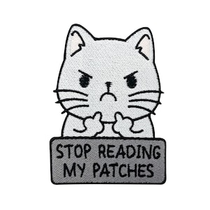 May include: An embroidered iron-on patch featuring a grey cat with angry eyebrows and crossed arms. The cat is holding a sign that says "Stop Reading My Patches".