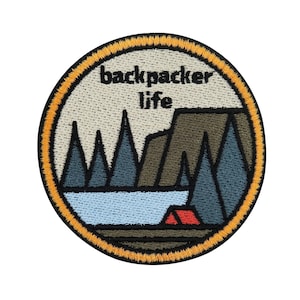 Puede incluir: Parche bordado con un diseño circular que presenta un lago, montañas, árboles y una tienda de campaña roja. El texto "backpacker life" está escrito en negro en la parte superior del parche.