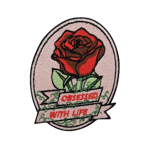 Puede incluir: Parche bordado para planchar con una rosa roja y hojas verdes en un marco ovalado rosa. La pancarta debajo de la rosa dice "Obsessed with Life".