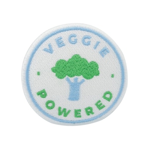 Può includere: Toppa rotonda bianca ricamata con cuciture blu. La toppa presenta un albero verde con un tronco blu e le parole "VEGGIE POWERED" in verde.