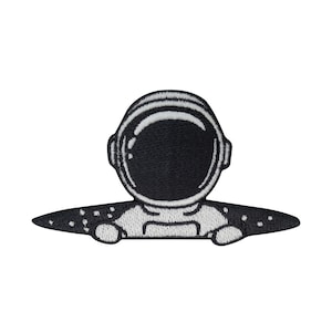 Pode incluir: Etiqueta bordada em preto e branco de um astronauta usando um capacete e olhando de trás de um fundo espacial estrelado preto e branco.