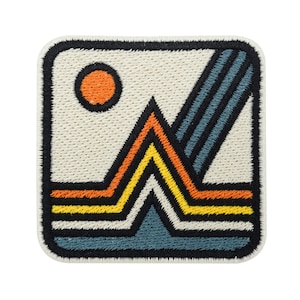 May include: A square embroidered patch with a white background and a black border. The patch features a stylised mountain scene with orange, yellow and blue lines. A small orange circle is in the top left corner.