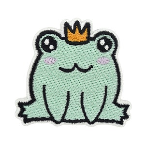 Może przedstawiać: Zielona haftowana żaba w złotej koronie. Żaba ma duże oczy i uśmiechnięte usta. Hafty są szczegółowe, a kolory są żywe.