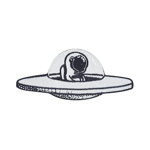 May include: Embroidered patch depicting a cartoon astronaut in a UFO. The patch is mainly white with black detailing, highlighting the astronaut's helmet and the spacecraft's outline. The design is simple and whimsical, ideal for clothing or accessories.