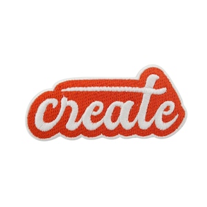 Op de afbeelding: Oranje stoffen patch met witte geborduurde tekst die "create" luidt.