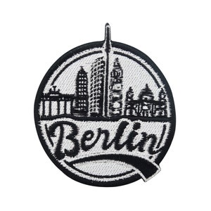 May include: Black and white embroidered patch with a cityscape of Berlin, Germany. The patch features the Brandenburg Gate, the Berlin TV Tower, and other iconic landmarks. The word "Berlin" is written in a stylized font below the cityscape.