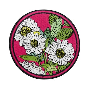 Può includere: Una toppa rotonda ricamata con uno sfondo rosa e margherite bianche con centri gialli. Le margherite sono circondate da foglie verdi.