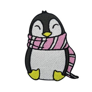 Pode incluir: Etiqueta bordada para passar a ferro de um pinguim de desenho animado a usar um cachecol rosa e branco listrado. O pinguim está a sorrir e tem pés amarelos.