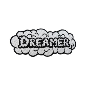 Può includere: Toppa ricamata in bianco e nero con la parola "DREAMER" in un font stilizzato, circondata da un design a nuvola.