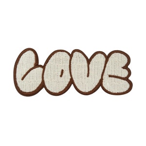 Könnte beinhalten: Ein brauner gestickter Aufnäher mit dem Wort "LOVE" in Weiß, mit einer leicht bauschigen Textur.