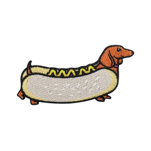 Op de afbeelding: Gestikt patch van een teckel die is verkleed als hotdog. De hond is bruin en de hotdog is geel met mosterd.