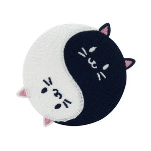 Op de afbeelding: Een geborduurde patch in zwart en wit van twee katten die een yin yang symbool vormen. De katten hebben roze oren en witte ogen.