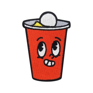 Könnte beinhalten: Roter Plastikbecher mit weißem Deckel und einem Comic-Gesicht. Der Becher hat große Augen, ein Lächeln und ein kleines gelbes Detail am Rand.