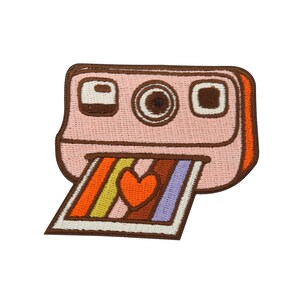 Könnte beinhalten: Ein gestickter Aufnäher mit einem rosa und braunen Sofortbildkamera, aus der ein regenbogenfarbenes Foto herauskommt. Das Foto hat ein rotes Herz in der Mitte.