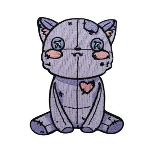 Könnte beinhalten: Ein gestickter Aufnäher mit einem lila Kätzchen, das ein rosafarbenes Herz auf der Brust trägt. Die Katze hat ein genähtes Aussehen und wirkt abgenutzt.