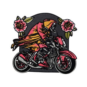 Könnte beinhalten: Gestickter Aufnäher mit einem Skelett, das ein Motorrad mit einem rosa-gelben Farbschema fährt. Das Skelett trägt einen Kapuzenumhang und das Motorrad hat ein florales Design.