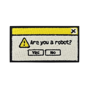 Könnte beinhalten: Ein gestickter Patch in Gelb und Schwarz mit einem Computerfenster-Design. Das Fenster hat eine gelbe Titelleiste mit einem roten X in der oberen rechten Ecke. Der Text "Sind Sie ein Roboter?" wird im Fenster angezeigt, zusammen mit einem gelben Warndreieck und zwei Schaltflächen mit der Beschriftung "Ja" und "Nein".
