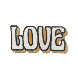 Könnte beinhalten: Ein weißer gestickter Aufnäher mit dem Wort "LOVE" im Retro-Stil. Die Buchstaben sind mit Schwarz, Orange, Rosa und Blau umrandet.