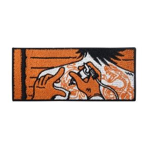 May include: An embroidered patch depicting a person receiving a tattoo. The tattoo artist is holding a tattoo gun and working on the person's arm. The tattoo design is a detailed dragon with orange and white accents.
