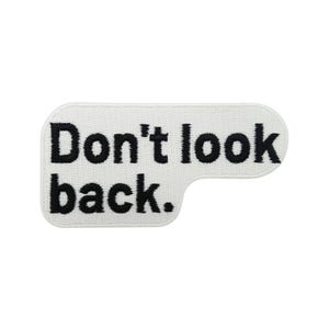Könnte beinhalten: Weißes rechteckiges Patch mit abgerundeten Ecken und dem Satz "Don't look back." in schwarzer, fetter, serifenloser Schrift. Das Patch hat eine strukturierte Oberfläche, was darauf hindeutet, dass es aus Stoff oder einem ähnlichen Material besteht.