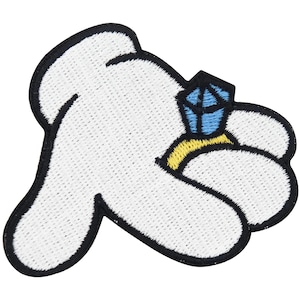 Könnte beinhalten: Gestickter Aufnäher mit einer weißen Cartoon-Hand mit schwarzer Umrandung, die einen Ring mit einem blauen Edelstein und einem gelben Band hält. Der Aufnäher ist zum Aufbügeln oder Aufnähen auf Stoff geeignet.