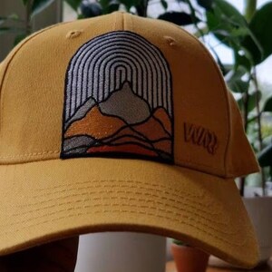 May include: A yellow baseball cap with an embroidered mountain scene and the word "Vuur" on the side.