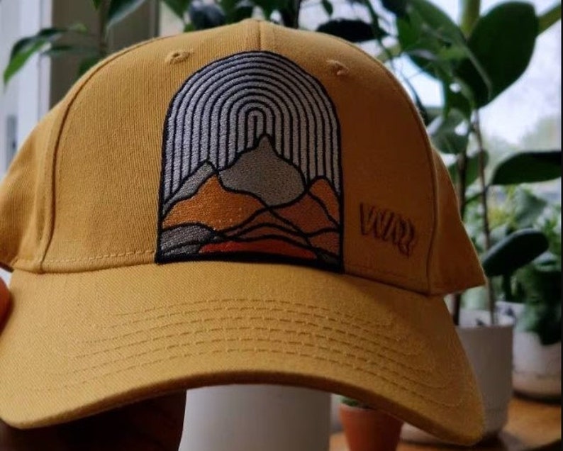 May include: A yellow baseball cap with an embroidered mountain scene and the word "Vuur" on the side.