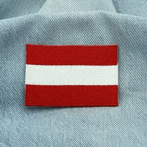 May include: A red and white embroidered patch of the Austrian flag on a blue denim background.