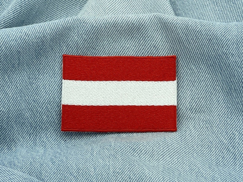 May include: A red and white embroidered patch of the Austrian flag on a blue denim background.