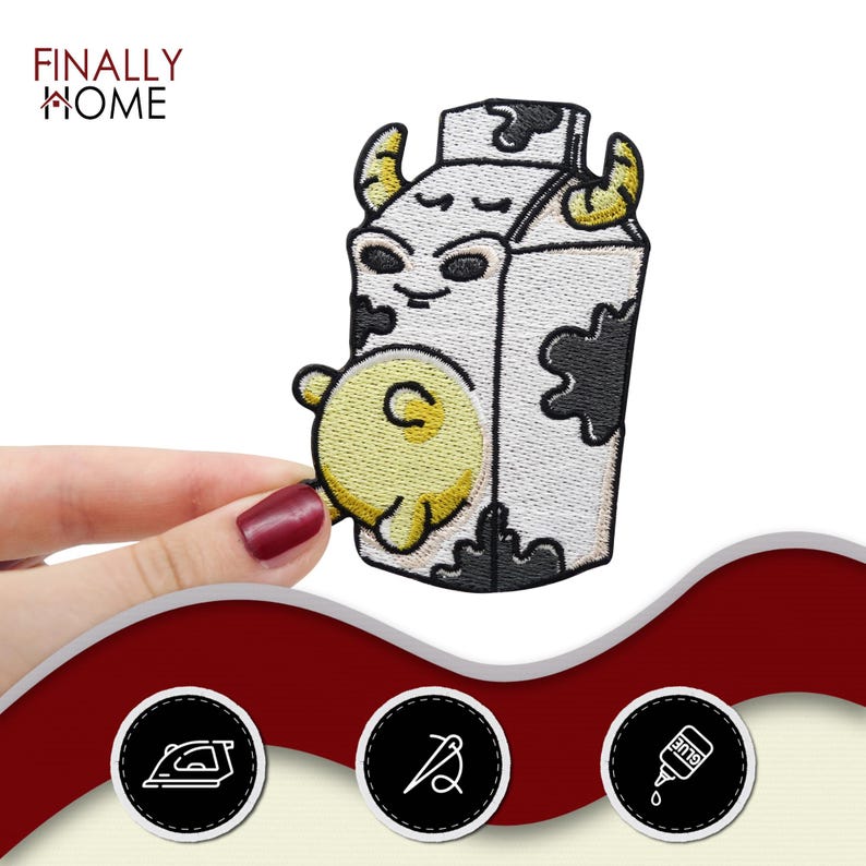 May include: A white cartoon milk carton with a black and white cow pattern. The carton has a cute face and a yellow cow udder. The carton is embroidered with black thread.