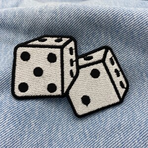 Pu&ograve; includere: Due dadi bianchi con punti neri, ricamati su un tessuto di jeans blu.