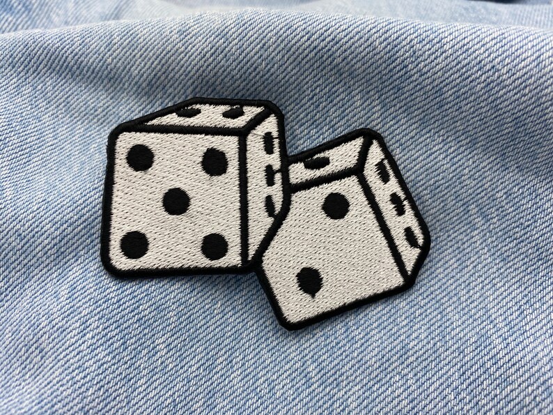 Pu&ograve; includere: Due dadi bianchi con punti neri, ricamati su un tessuto di jeans blu.