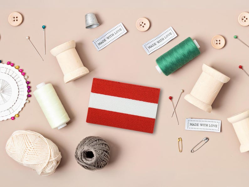 May include: A flat lay of sewing supplies, including spools of thread, buttons, pins, and a thimble. There is also a small fabric flag of Austria with the text "Made with Love" on three labels.
