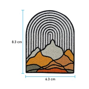 May include: An embroidered patch featuring a mountain range design. The mountains are in shades of orange, brown, and grey, with a white and black striped arch above them. The patch measures 6.3 cm wide and 8.3 cm high.