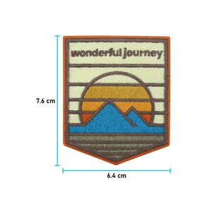 May include: An embroidered patch with a sunset, mountains, and the text "wonderful journey". The patch is 6.4 cm wide and 7.6 cm tall.