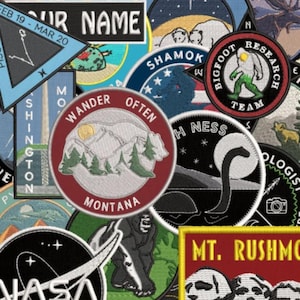 May include: A collection of embroidered patches with various designs and text. Patches include a Bigfoot Research Team logo, a Montana landscape with text "Wander Often Montana", and a NASA logo. Other patches feature text like "Your Name" and "H Ness".